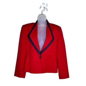 Pode incluir: Um blazer vermelho com uma borda preta ao redor do colarinho e dos bolsos. O blazer tem um fecho de botão único.