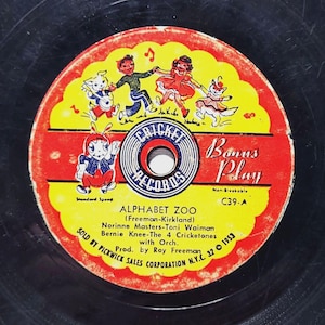 May include: A red and yellow vinyl record with a picture of children dancing and a cricket character. The record is titled "Alphabet Zoo" and is a "Bonus Play" record by Cricket Records. The record is non-breakable and has the number C39-A. The record was sold by Pickwick Sales Corporation in 1953.