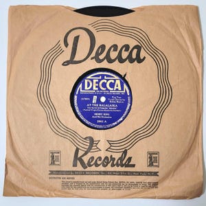 May include: A vintage Decca Records 78 RPM record in its original brown paper sleeve. The record label is blue with white text, featuring the title "At The Balalaika" by Henry King and His Orchestra. The sleeve has the Decca Records logo.