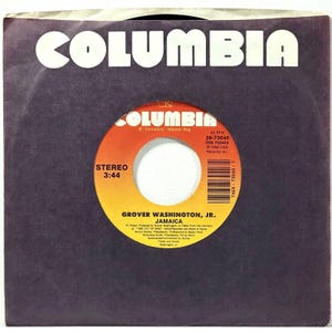 May include: A vintage 45 RPM record in a black sleeve. The record label is orange and yellow with the text "COLUMBIA" and "GROVER WASHINGTON, JR. JAMAICA". The sleeve has the word "COLUMBIA" in white.
