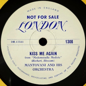 May include: A white vinyl record with black text that reads "MADE IN ENGLAND", "NOT FOR SALE", "LONDON", "DR.17511", "KISS ME AGAIN", "from "Mademoiselle Modiste"", "(Herbert, Blossom)", "MANTOVANI AND HIS ORCHESTRA", "1308", and "UNAUTHORIZED PUBLIC PERFORMANCE, BROADCASTING AND COPYING OF THIS RECORD PROHIBITED".
