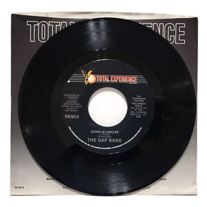 May include: A black vinyl record with the title "Going in Circles" by The Gap Band. The record is a remix and was produced by L. Simmons and J. Ellis. The record is from the album "Gap Band T" and was released by Total Experience Records in 1986.