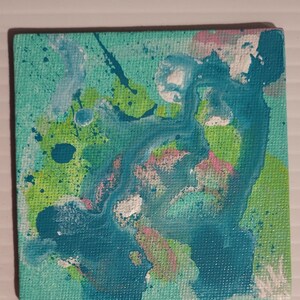 May include: Square abstract painting with a teal background and splashes of blue, green, pink, and white. The artwork features a textured canvas and a vibrant, colorful design. The painting is a small square, perfect for wall decor.
