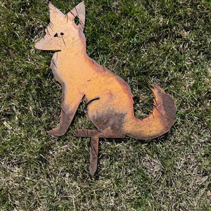 Puede incluir: Una estaca de jard&iacute;n de metal oxidado en forma de silueta de zorro. El zorro est&aacute; sentado con la cola enroscada alrededor de su cuerpo. La estaca est&aacute; insertada en el suelo.