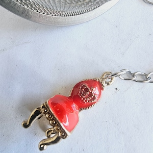 Könnte beinhalten: Ein roter und goldener Tee-Infuser in Form eines Stuhls mit einer Kette.