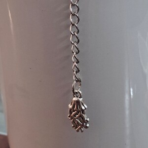 May include: A silver tea infuser with a chain and a decorative design that resembles a hand.