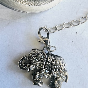 May include: Silver tea infuser with a chain and a silver elephant charm decorated with rhinestones.
