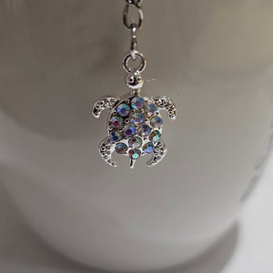 Könnte beinhalten: Silberfarbener Tee-Infuser in Form einer Schildkröte, verziert mit schillernden Strasssteinen. Der Schildkröten-Anhänger hängt an einer filigranen Kette. Zum Aufbrühen von Tee in einer Tasse.
