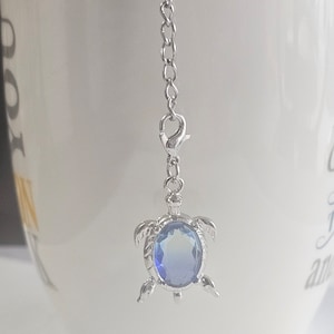 Può includere: Una catena d'argento con un ciondolo a forma di tartaruga in cristallo blu. La tartaruga è un simbolo popolare di buona fortuna e longevità.