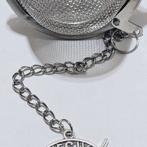 Puede incluir: Un infusor de té de plata con una cadena y un amuleto con forma de pez con la palabra "JESUS" inscrita en su interior.