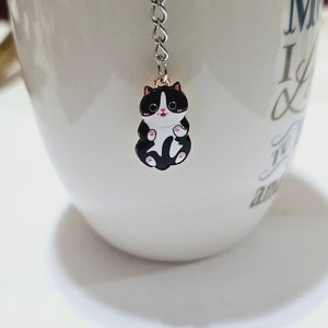 May include: A white ceramic mug with a black and white cat tea infuser hanging from the rim. The mug has the text "Mom I Love You" printed on the side.