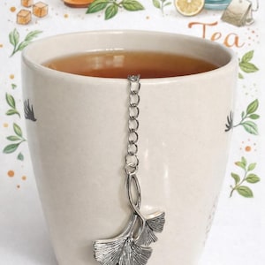May include: A white ceramic mug with a black handle and the text "But First, Coffee" in a bold, black font. The mug is set against a neutral background, highlighting its simple design.