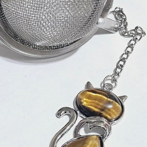 May include: A silver tea infuser with a mesh ball and a chain attached to a tiger's eye cat charm.