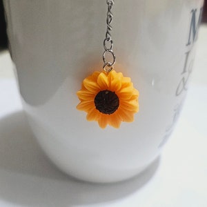 May include: A white ceramic mug with a silver chain and a yellow sunflower charm hanging from the rim. The mug has the words "My Love" written on the side.