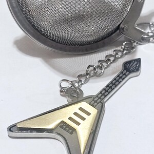 May include: A silver tea infuser shaped like a guitar with a gold body and black details. The infuser has a chain and a round mesh ball with the text "SUS304" on the side.