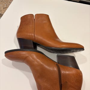 May include: A pair of brown leather ankle boots with a pointed toe and a block heel. The boots have a zipper closure on the side and are made of a smooth, polished leather. The heel height is approximately 3 inches.