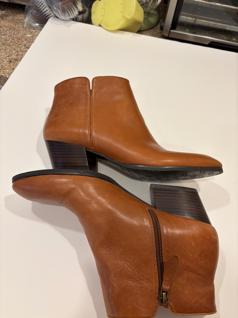 May include: A pair of brown leather ankle boots with a pointed toe and a block heel. The boots have a zipper closure on the side and are made of a smooth, polished leather. The heel height is approximately 3 inches.