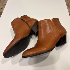 May include: A pair of brown leather ankle boots with a side zipper and a block heel. The boots have a pointed toe and a dark brown sole. The leather has a slight sheen.