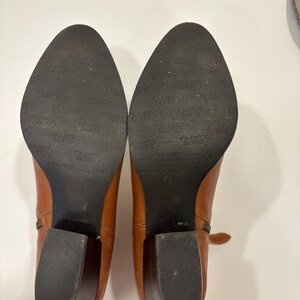May include: A pair of brown leather ankle boots with a block heel. The soles are black and feature the brand name "FRANCO SARTO". The boots are set against a white background.