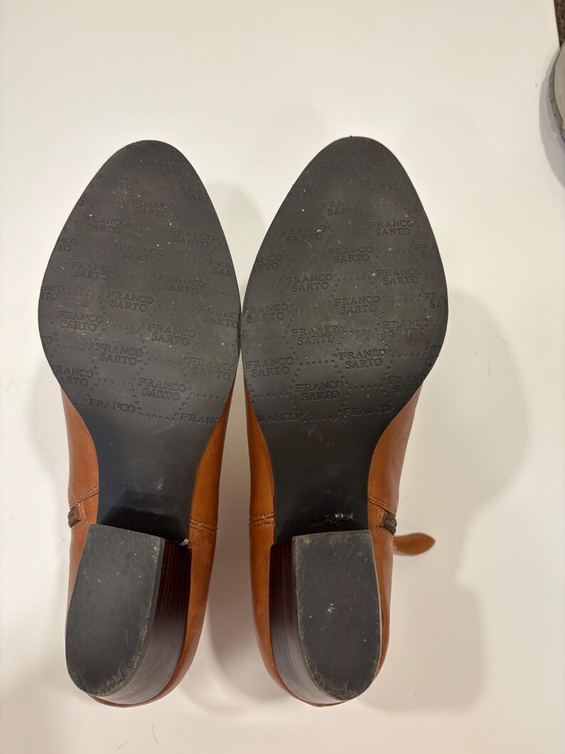 May include: A pair of brown leather ankle boots with a block heel. The soles are black and feature the brand name "FRANCO SARTO". The boots are set against a white background.