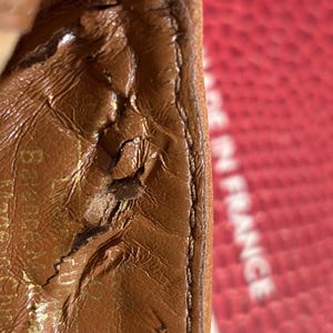 May include: Close-up of a brown leather item with visible wear and tear. The text "Made in France" is partially visible in the background. The leather has a textured surface and a stitched edge.