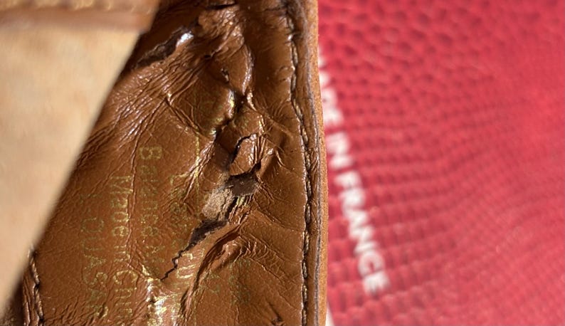 May include: Close-up of a brown leather item with visible wear and tear. The text "Made in France" is partially visible in the background. The leather has a textured surface and a stitched edge.