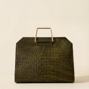 Puede incluir: Bolso de mano verde oliva estructurado, de forma rectangular, con un asa rectangular dorada. El bolso presenta un patrón texturizado con forma de piel de cocodrilo. El asa está fijada en la parte superior.