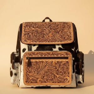 Könnte beinhalten: Ein Rucksack im Western-Stil mit Kuhfellmuster und geprägten Lederakzenten. Die Klappe und die Vordertasche weisen aufwendige florale Designs auf. Die Tasche hat Seitentaschen und einen oberen Griff. Die Farbpalette umfasst Braun, Schwarz und Weiß.