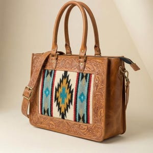 May include: A brown leather tote bag with a Southwestern-style patterned fabric panel. The bag features a floral embossed design, a top zipper, two handles, and an adjustable shoulder strap. The fabric panel has a geometric design with blue, red, and yellow accents.