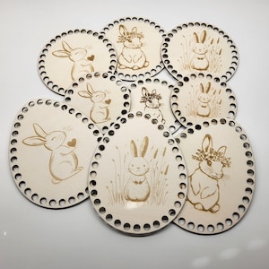 May include: A selection of wooden Easter basket bases with laser-etched bunny designs. The bases are oval and circular, featuring bunnies with floral crowns, hearts, and in grassy settings. Each base has small holes around the edge.