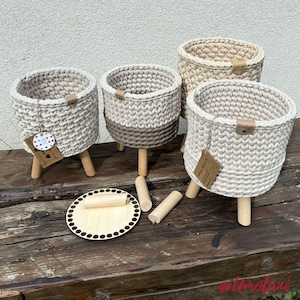 Può includere: Quattro cesti all'uncinetto fatti a mano in varie tonalità di beige e grigio, ciascuno con gambe in legno. Un cesto ha un design bicolore. Sono presenti anche una base in legno e gambe in legno aggiuntive. Ogni cesto ha una piccola etichetta.