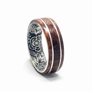 May include: A wooden ring with two silver bands and a floral design engraved on the inside.