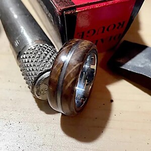 May include: A brown wooden ring with a silver band and a thin silver line around the edge. The ring is sitting on a wooden surface.