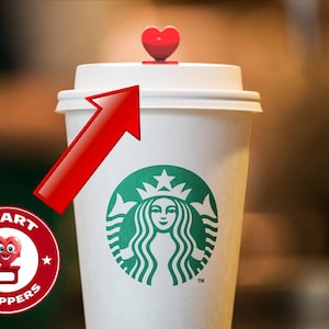 May include: A white paper coffee cup with the Starbucks logo, topped with a white lid and a red heart-shaped stopper. The image includes a red arrow pointing to the stopper and a circular graphic that says "HEART STOPPERS".
