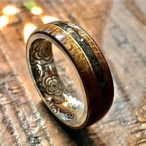 May include: A wooden ring with a black and gold inlay. The ring has a floral pattern engraved on the inside.