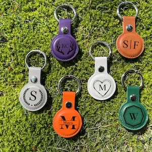 Pode incluir: Seis chaveiros de couro diferentes com iniciais e designs personalizados. Os chaveiros são de várias cores, incluindo roxo, marrom, branco, laranja e verde. As iniciais nos chaveiros são KC, S/F, M, S, M e W.