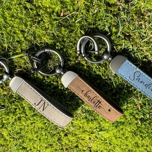 Op de afbeelding: Drie leren sleutelhangers met metalen ringen. De sleutelhangers zijn gepersonaliseerd met de namen "Sandie", "Charlotte" en "JN".