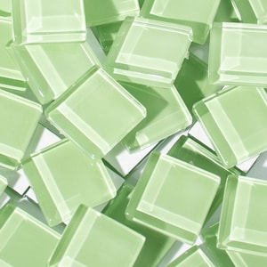 May include: A pile of light green glass mosaic tiles. The tiles are square and have a slightly frosted finish.
