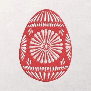 May include: A red Easter egg with white embroidered floral and geometric patterns. The egg features a central flower design and radiating lines, with smaller leaf-like accents. The design is set against a white background.