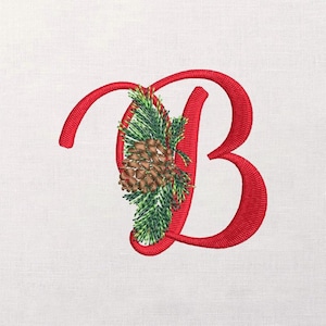 Könnte beinhalten: Gestickter roter Buchstabe "B" mit festlichem Design. Der Buchstabe ist mit einem detaillierten Tannenzapfen und immergrünen Zweigen verziert, wodurch ein saisonales oder festliches Thema entsteht. Das Design befindet sich auf weißem Hintergrund.