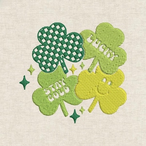 以下が含まれることがあります： 緑と黄色の四つ葉のクローバーの刺繍デザイン。「Lucky」と「Stay Gold」の文字入り。 クローバーの葉はテクスチャ加工が施され、星型のアクセントで囲まれています。ニュートラルな背景に配置されています。