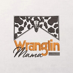 May include: Embroidered design with a cow skull and a black and white cowhide pattern within a rectangular frame. The text "Wranglin Mama" is in orange and black, with a stylized font. The design is on a white fabric.