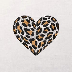 Puede incluir: Corazón bordado con un estampado de leopardo en negro, marrón y blanco. La forma de corazón está centrada sobre un fondo blanco, mostrando los detalles de la costura y el diseño.