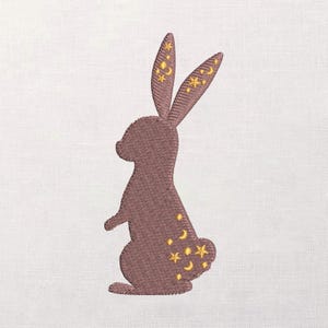 May include: Embroidered design of a brown rabbit with yellow stars and crescent moons. The rabbit is standing on its hind legs, with the stars and moons decorating the ears and the lower back. The background is a plain white fabric.