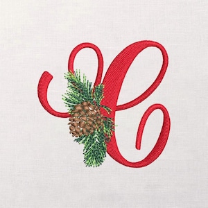 Puede incluir: Letra "C" roja bordada con una piña y ramitas de hoja perenne. El diseño presenta una fuente cursiva con un tema festivo. La piña es marrón y la hoja perenne es verde. El fondo es una tela blanca lisa.