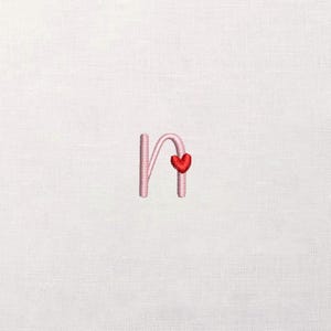 May include: Embroidered pink letter "n" with a red heart accent. The cursive style initial is stitched on a white fabric background. The design is simple and elegant, suitable for personalized items.