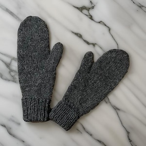 May include: A pair of grey knitted mittens with a textured surface. The mittens have a fold-over cuff.
