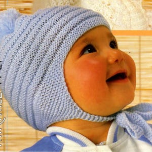 May include: A light blue knitted baby hat with a pom pom on top and a tie at the neck. The hat is made with a simple stitch pattern and has a fold-over brim. The hat is worn by a baby with rosy cheeks.