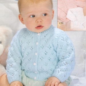 May include: A baby wearing a light blue knitted cardigan with a delicate lace pattern. The cardigan has a button closure and is made with a soft yarn.