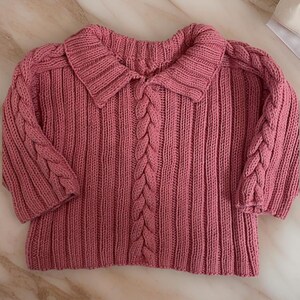 May include: A pink knitted sweater with a cable knit pattern and a collared neckline.